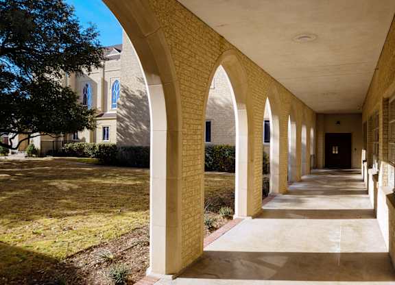 A long corridor with arched columns and a building in the background.