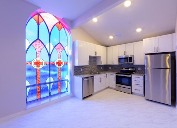 A kitchen with a stained glass window and white cabinets.