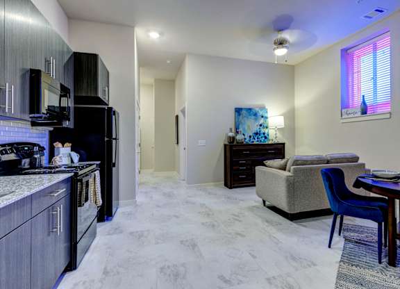 A modern kitchen with a black refrigerator and a dining area with a blue chair.