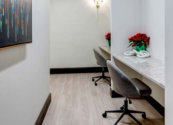 A hallway with a painting on the wall, a table with chairs and flowers on it, and a whiteboard.