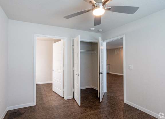 A room with a ceiling fan and three open doors.