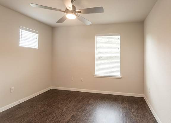 A room with a ceiling fan and two windows.