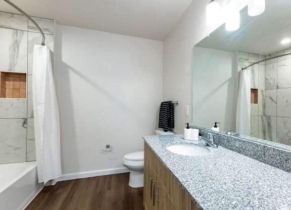 A white toilet sits in a bathroom with a marble counter top and a white shower curtain.