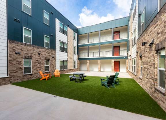 A courtyard with a lawn and chairs in front of a building.