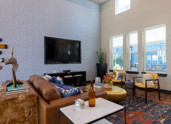 A living room with a brown couch, a white coffee table, and a flat screen TV mounted on the wall.