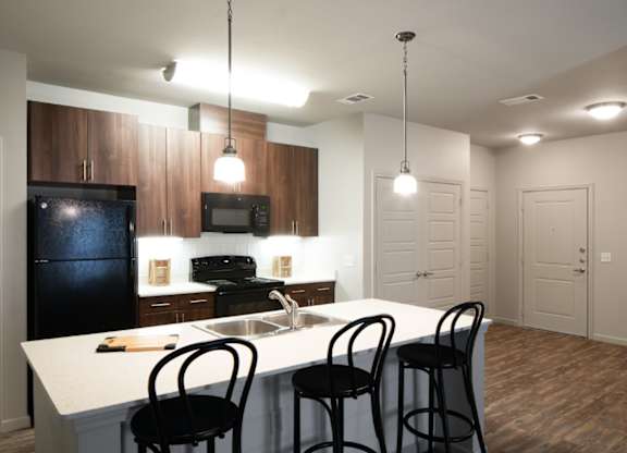 A kitchen with a black fridge, white countertop, and black barstools.