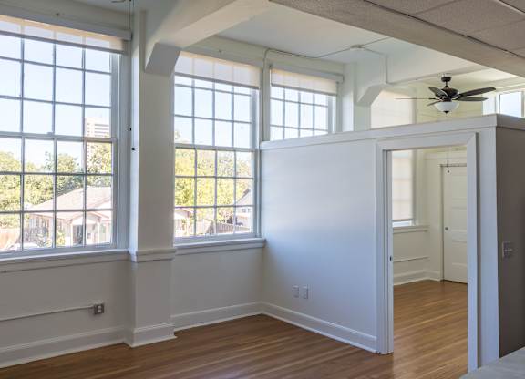 A room with a ceiling fan and large windows.