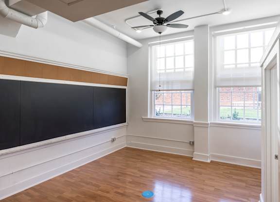 A room with a ceiling fan and a blackboard on the wall.