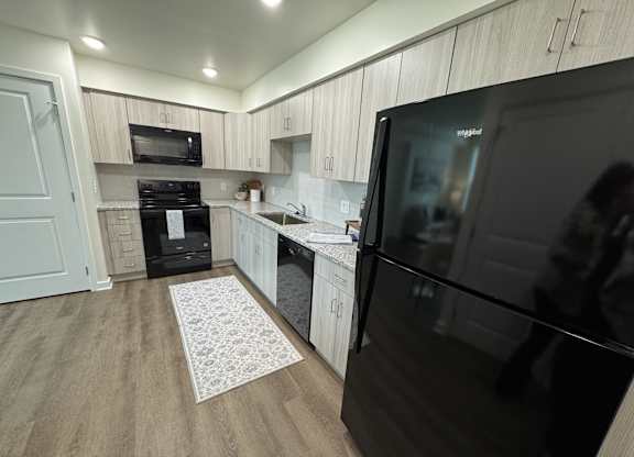 A modern kitchen with a black fridge and wooden cabinets.