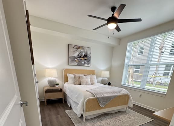 A bedroom with a bed, a ceiling fan, and a window with blinds.