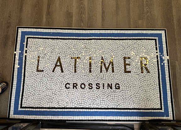 A mosaic sign that says "Latimer Crossing" is displayed on a wooden surface.