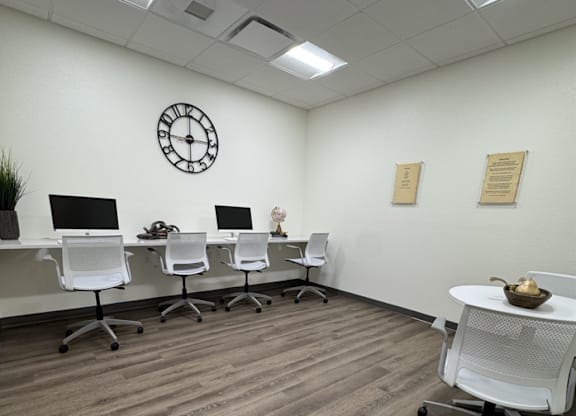 A white office with a clock on the wall and chairs around a table.