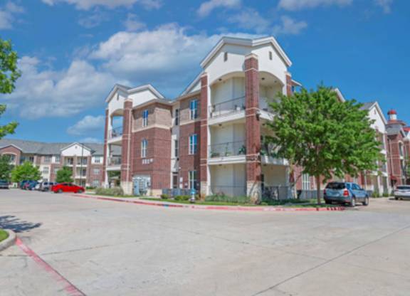 A large red brick apartment building with a parking lot in front.