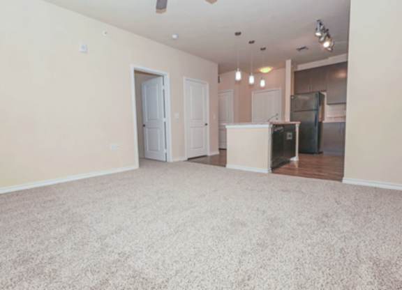 A sparsely furnished living room with a kitchen in the background.