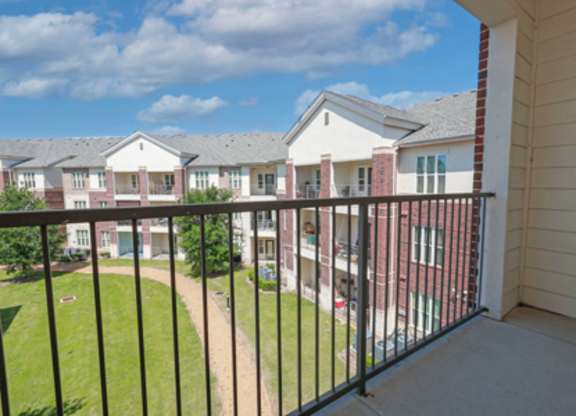 A balcony overlooks a grassy area and apartment buildings.