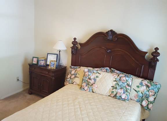 A bed with a floral pillow and a wooden headboard sits in a room with a nightstand and lamp.