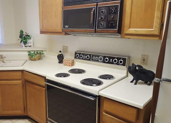 A kitchen with a black cat sitting on the stove.