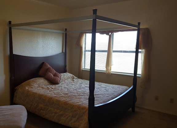 A bed with a white pillow and a white blanket is in the corner of a room.