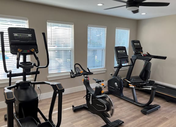 Three exercise bikes are lined up in a room with a ceiling fan.