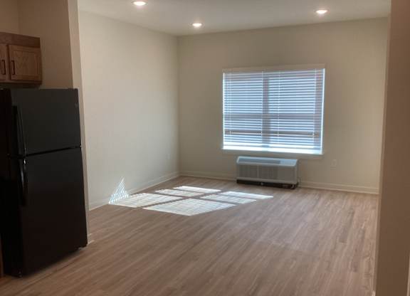 A room with a black fridge and wooden flooring.