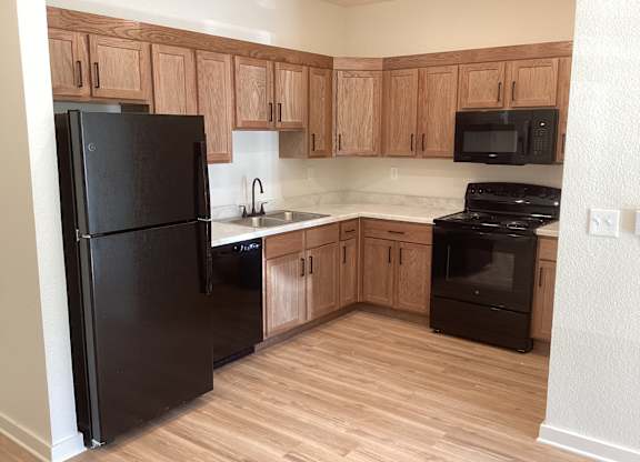 A black refrigerator is in a kitchen with wooden cabinets.
