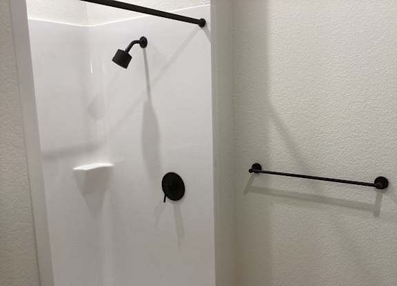 A white shower stall with a black shower head and a black bar.