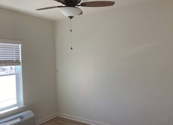 A room with a ceiling fan and a window with blinds.