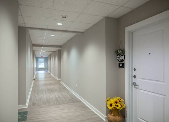 A long hallway with a door on the right and a vase of flowers on the floor.