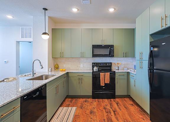 A kitchen with black appliances and green cabinets.