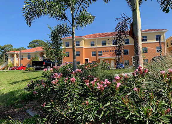 A building with orange walls and a red roof is surrounded by greenery and trees.