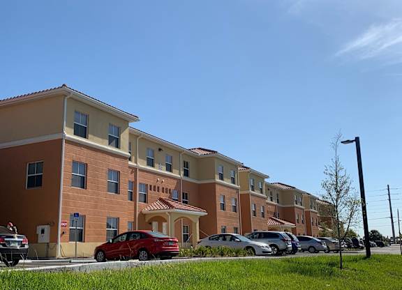 A red car is parked in front of a building with a parking lot.