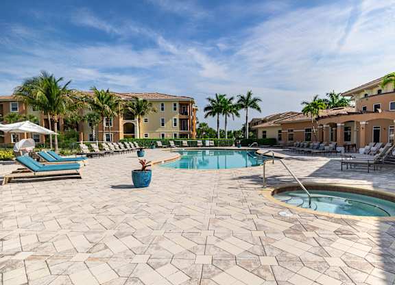 A pool surrounded by a patio with chairs and umbrellas.