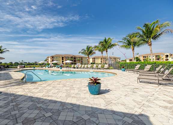 A pool surrounded by palm trees and lounge chairs.
