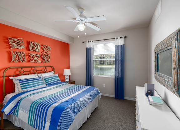 A bedroom with a bed, a ceiling fan, and a window with blue curtains.