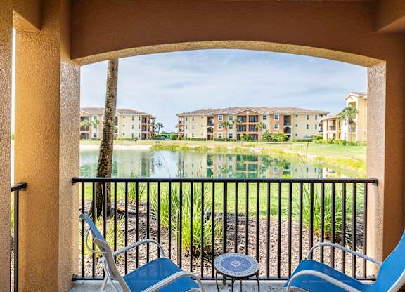 A balcony with two chairs and a table overlooks a body of water and buildings.