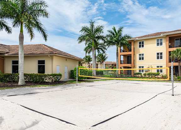 A tennis court is in the foreground of a residential area with apartment buildings and palm trees.