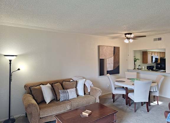 A living room with a brown couch, a coffee table, and a dining table with chairs.