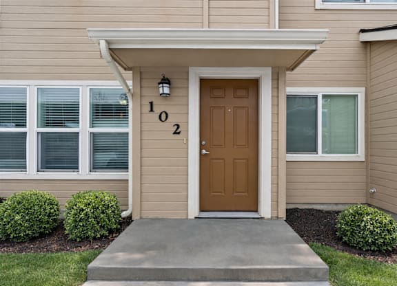 A beige house with a brown door and number 102 on the wall.