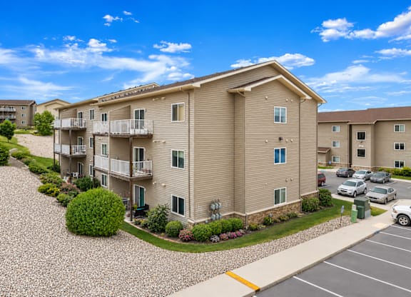 A sunny day at a residential complex with apartment buildings and cars parked in the lot.