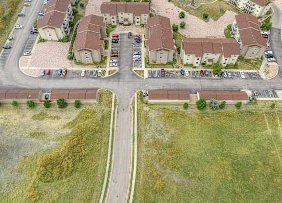 A road with cars parked on the side and houses in the background.