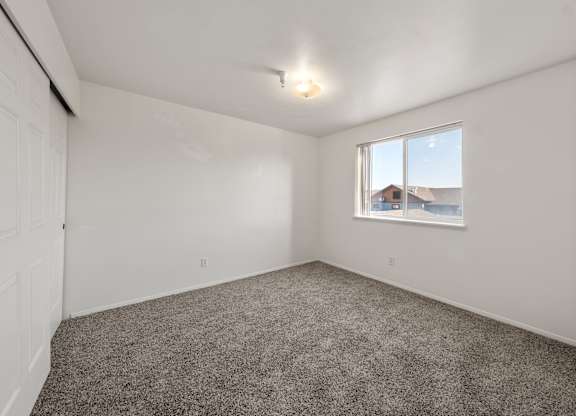 A room with a carpeted floor and a window showing a view of a house.