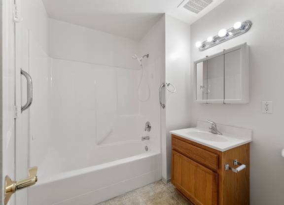 A white bathroom with a wooden vanity and a glass shower door.