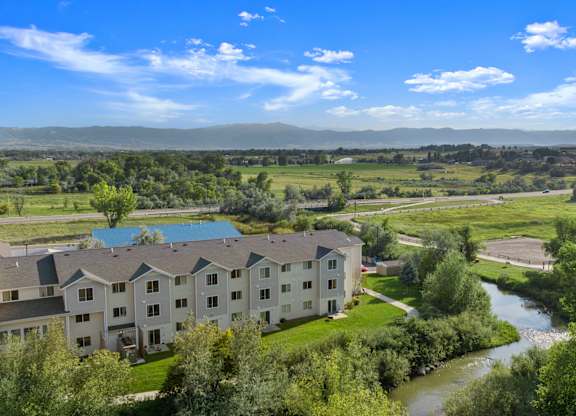 A river flows through a green valley with apartment buildings on the left.