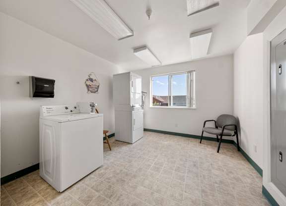 A laundry room with a washer and dryer, a chair, and a window.