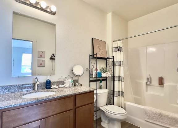 A bathroom with a sink, mirror, toilet, and shower.