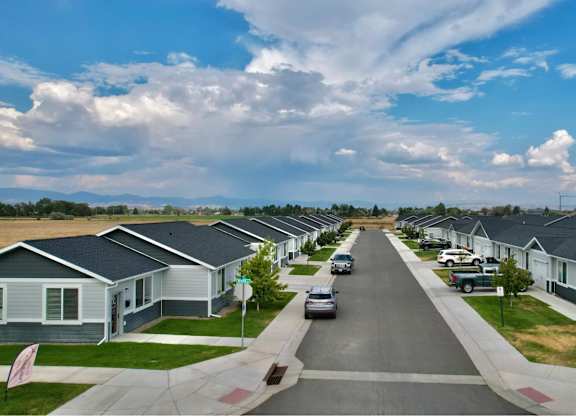 A street view of a residential area with houses on both sides and cars parked on the side of the road.