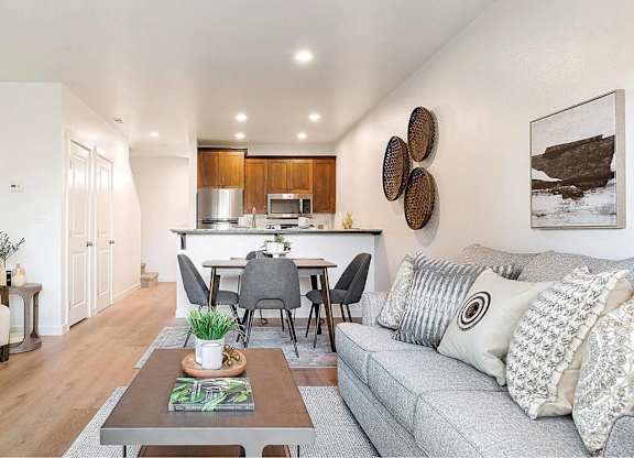 A modern living room with a grey sofa, wooden dining table, and a white chair.