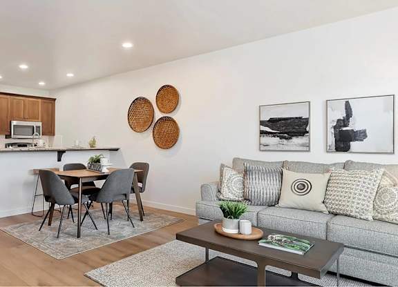 A modern living room with a grey couch, a dining table with chairs, and a kitchen area in the background.