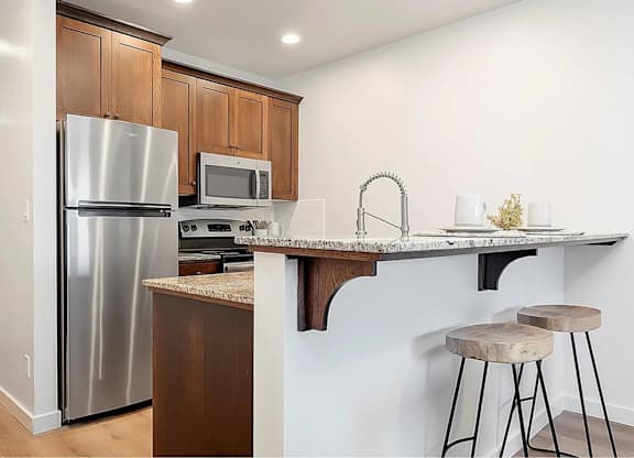 A kitchen with a refrigerator, microwave, and bar stools.