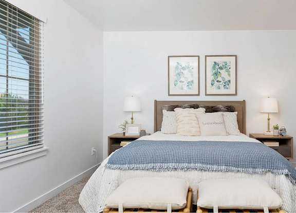 A bedroom with a bed, two lamps, and two framed pictures on the wall.